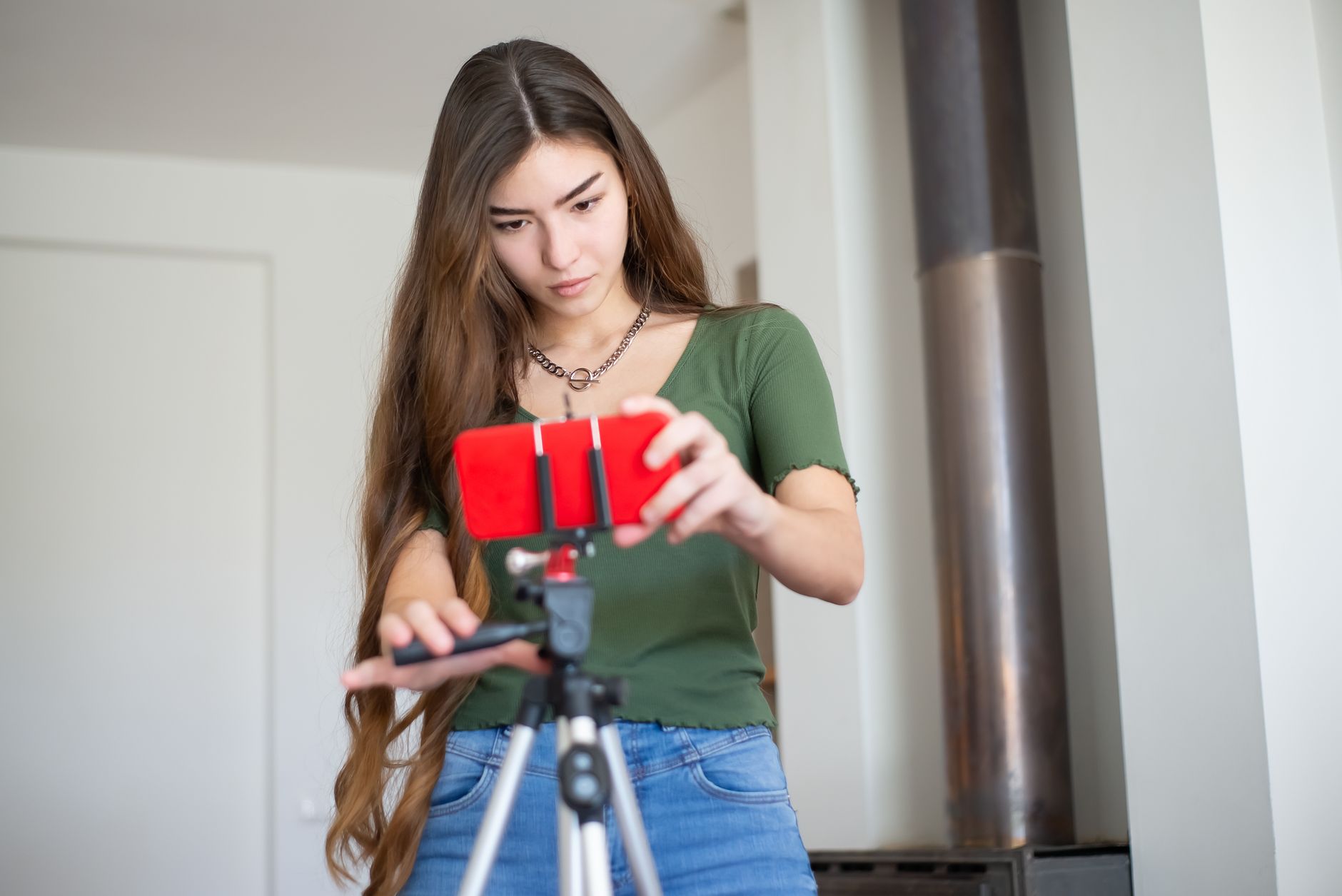 Jeune femme ajustant son smartphone sur un trépied à l'intérieur, en train de préparer un tournage.