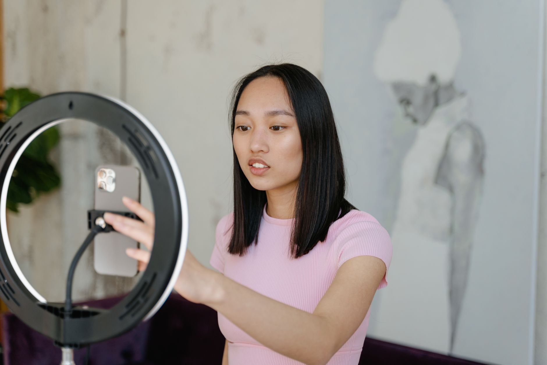 Jeune femme utilisant un smartphone et un anneau lumineux pour créer du contenu à la maison.